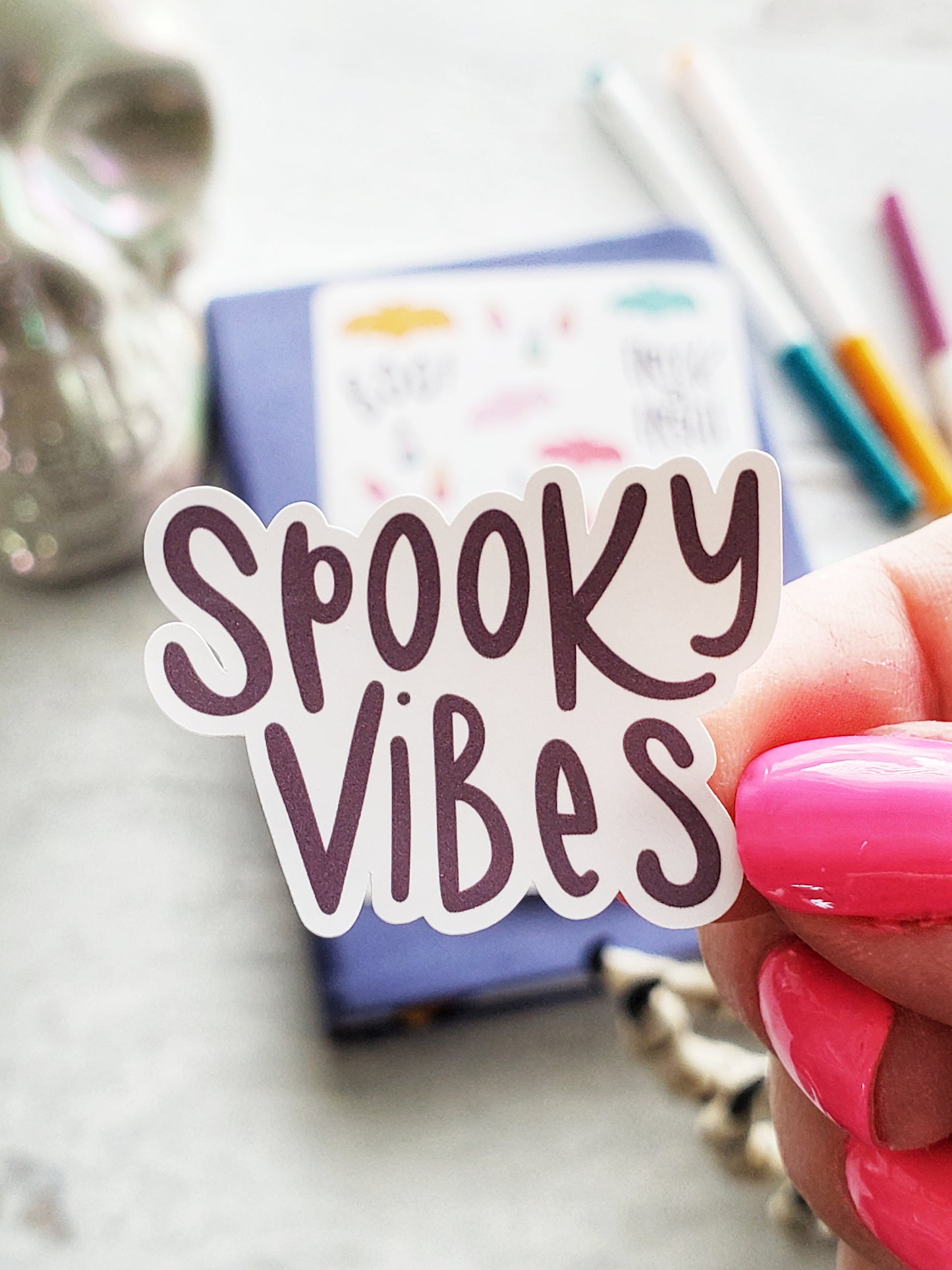 Close up of a sticker that says "Spooky Vibes" in dark purple hand drawn text.