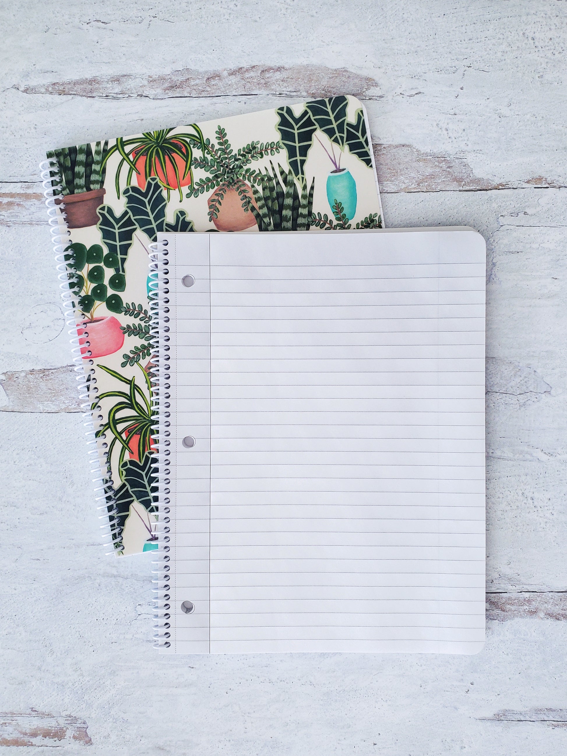 open spiral notebook showing lined pages resting on top of a notebook with illustrated house plants pattern to show the cover design
