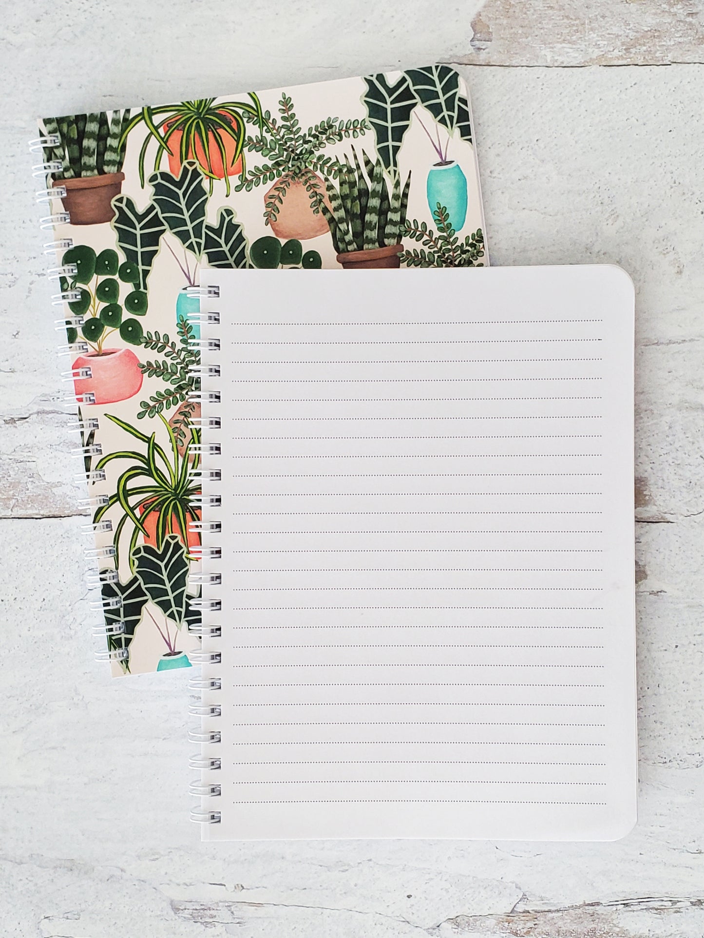 notebook opened to show lined pages on top of closed notebook showing cover with house plants pattern