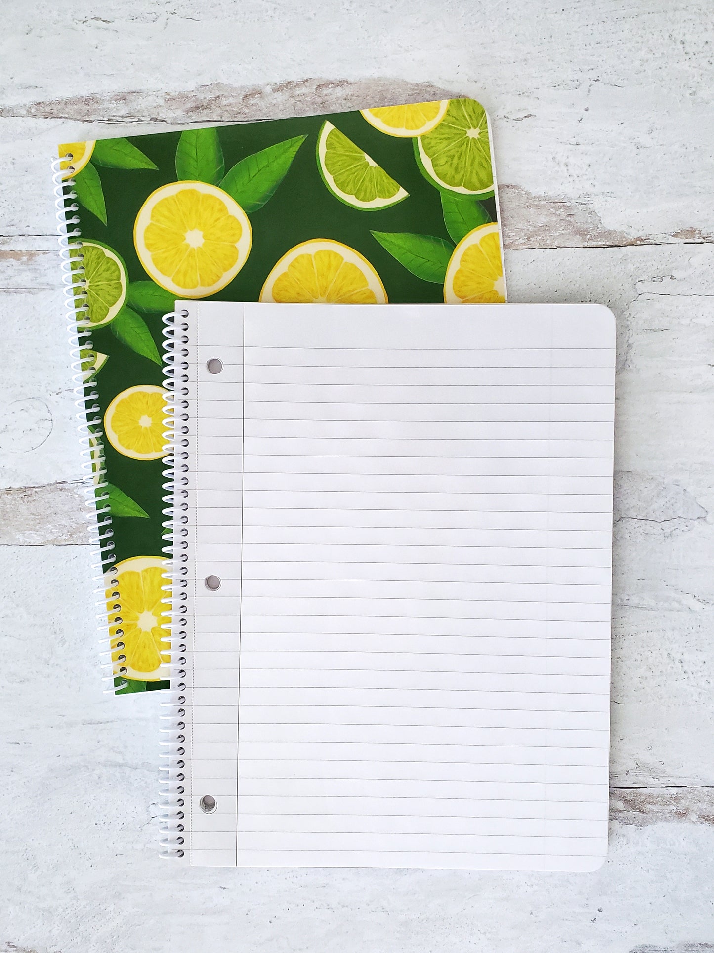 open spiral notebook showing lined pages resting on top of a dark green notebook with lemon and lime slice pattern to show the cover design
