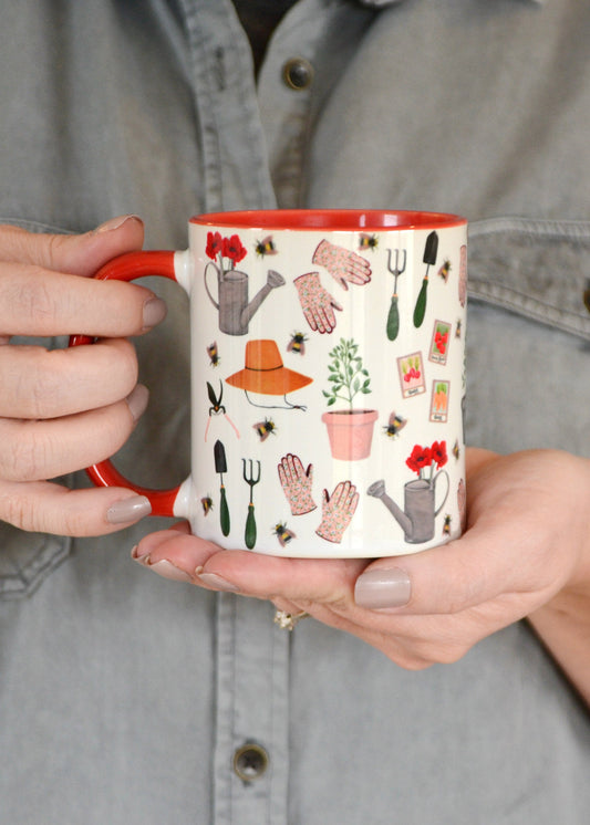 ceramic mug with red handle and interior wrap around pattern is hand painted gardening inspired illustrations on white background