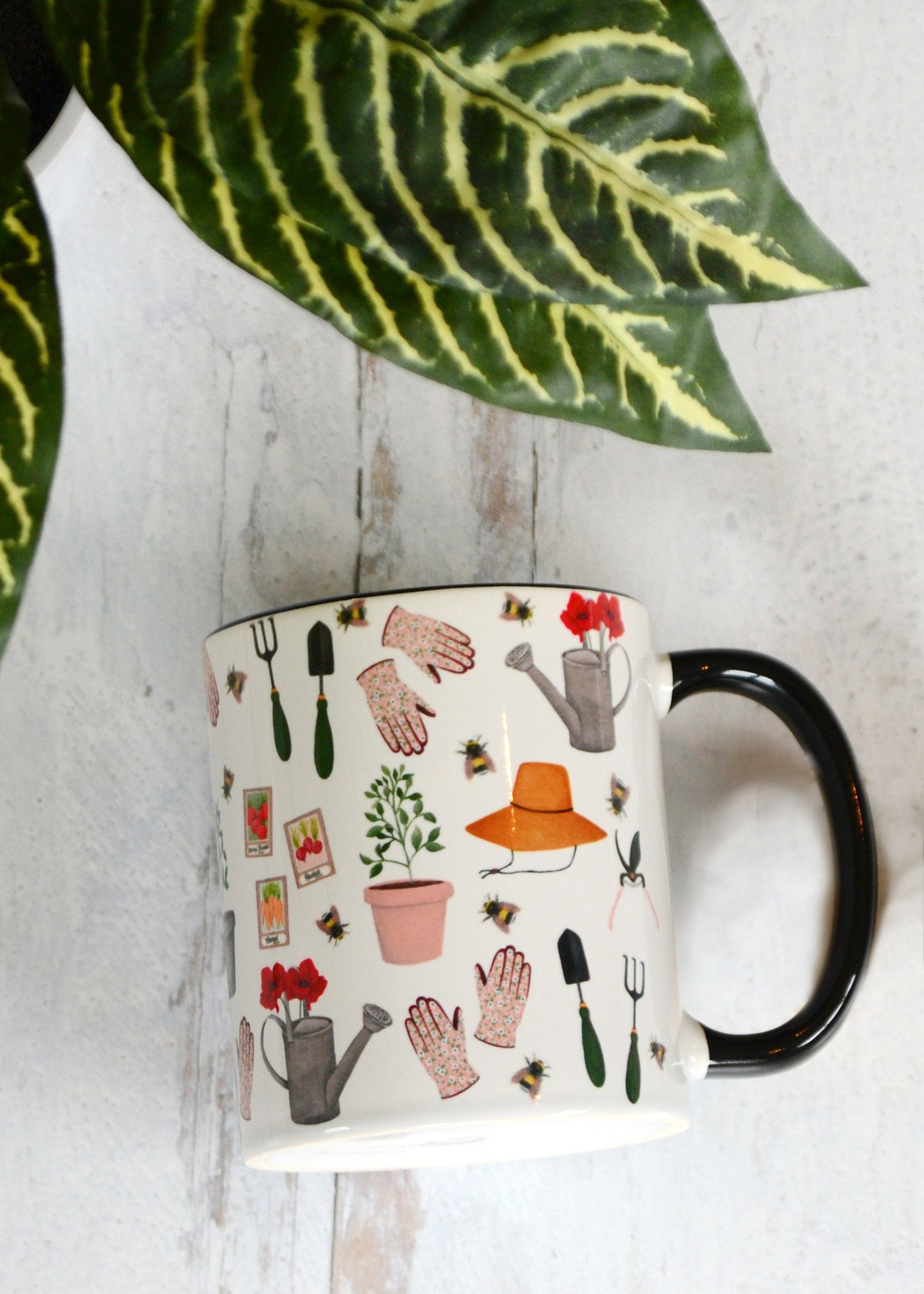 gardening mug with black handle laying on white weathered with plant leaves
