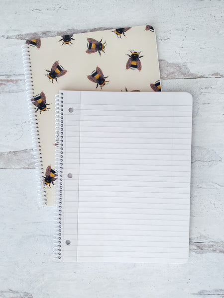 open spiral notebook showing lined pages resting on top of a notebook with bumble bee pattern to show the cover design