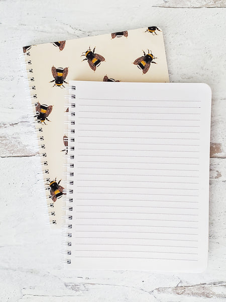 notebook flipped open to show lined pages on top of closed notebook showing cover with bee pattern 
