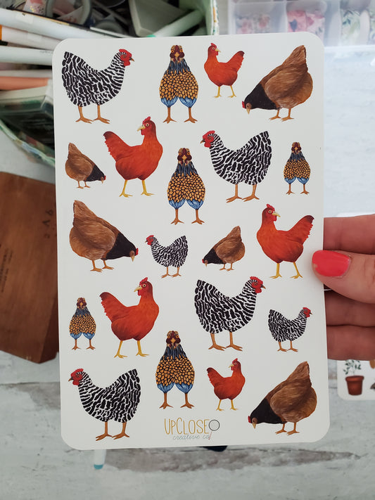 A sticker sheet full of hand painted chicken art in various sizes. There is a brown, red, black and white and blue and yellow chicken.