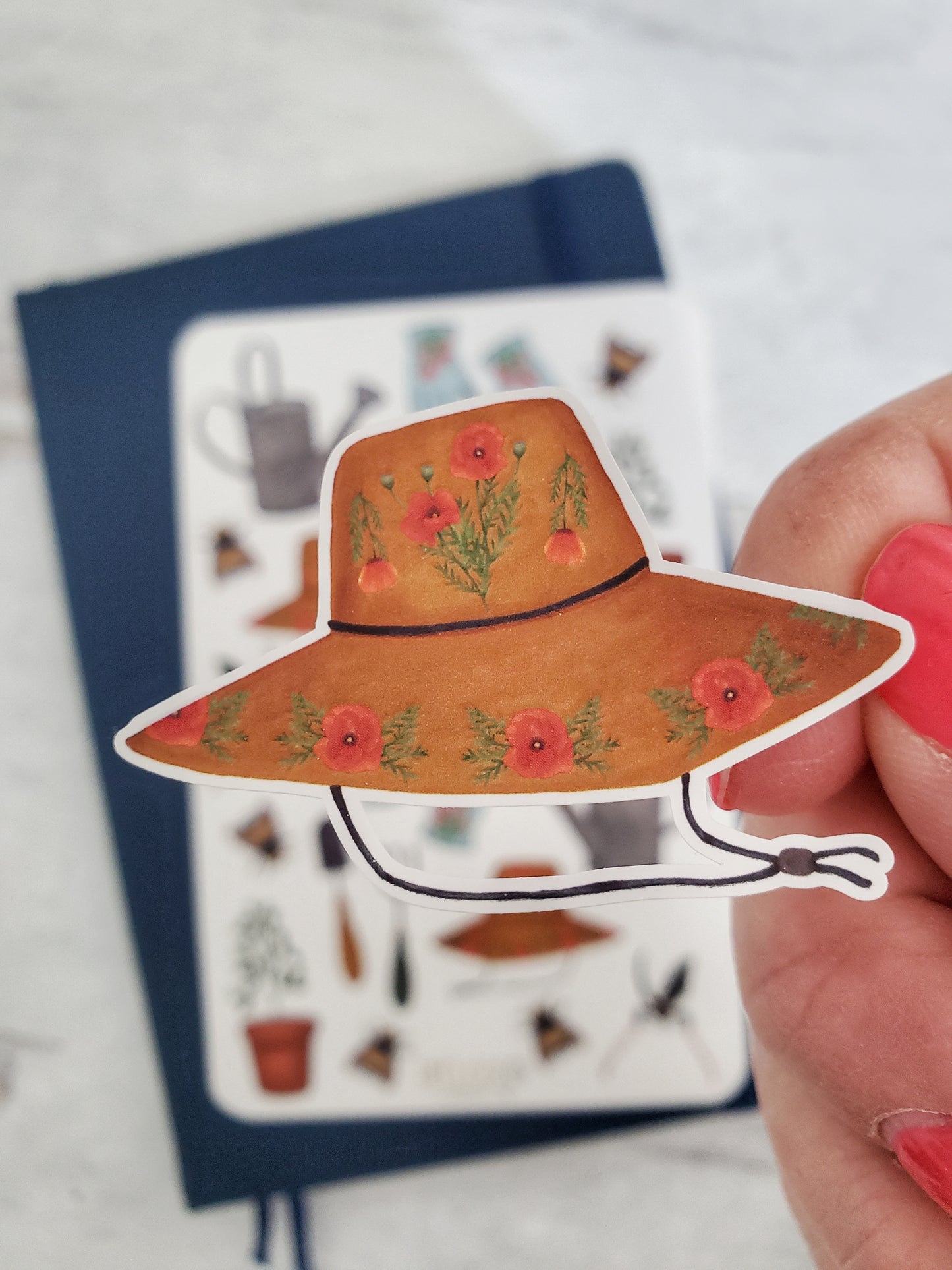 A close up of the gardening hat sticker. There are small poppy flower details on the hat which is brown. 