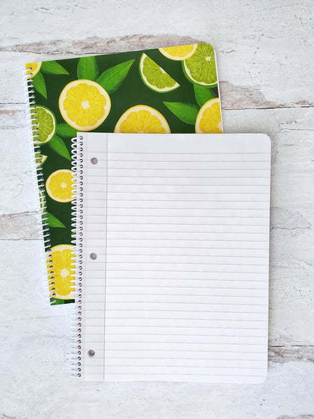 open spiral notebook showing lined pages resting on top of a dark green notebook with lemon and lime slice pattern to show the cover design