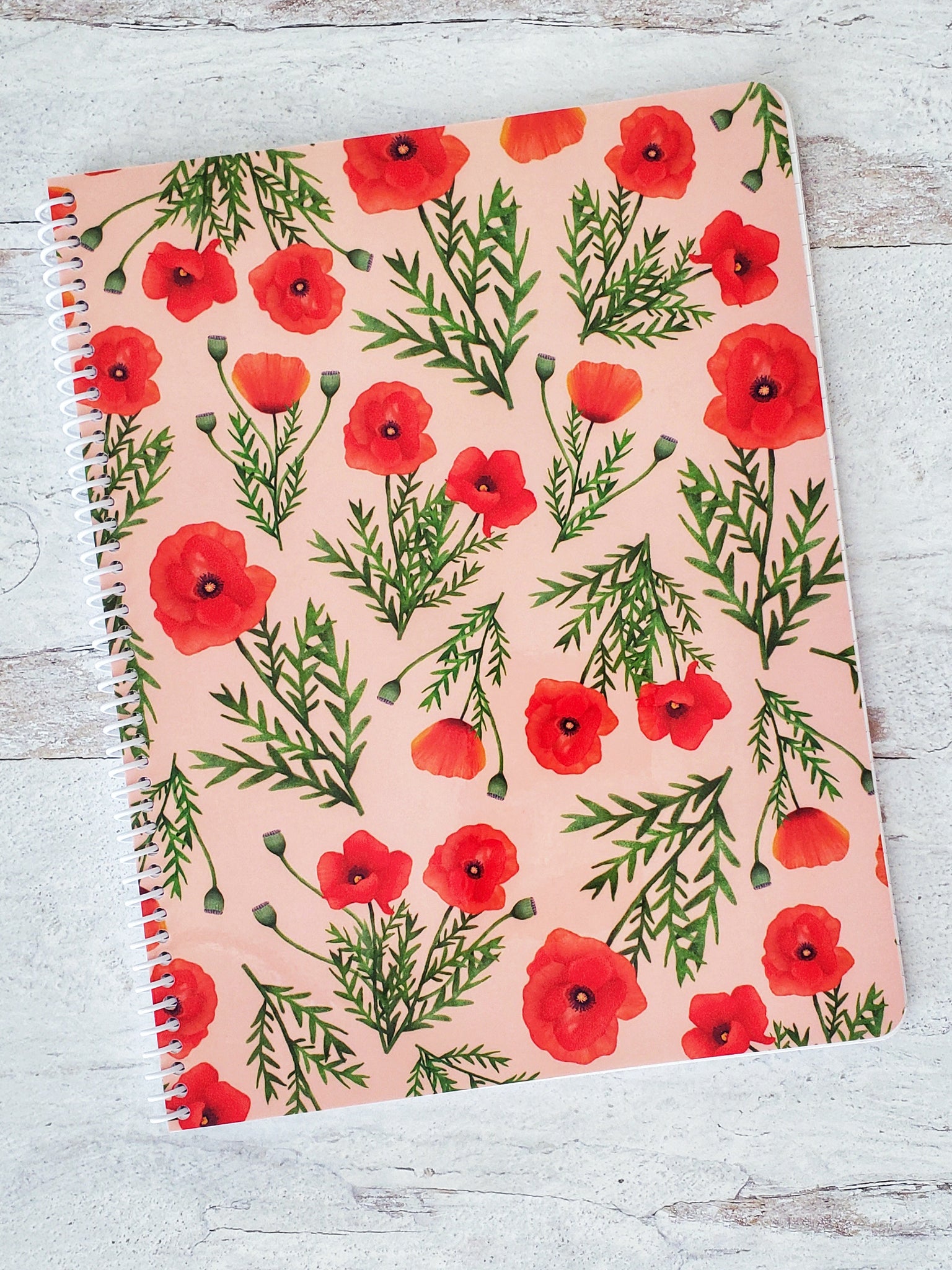 spiral notebook with light pink background and illustrated red poppies pattern on cover