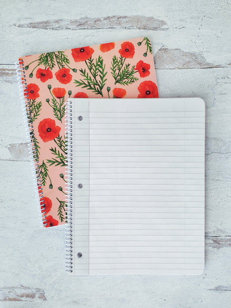 open spiral notebook showing lined pages resting on top of a pink notebook with red poppies to show the cover design