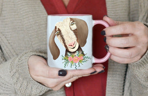 ceramic mug with pink handle and interior features hand painted white and brown goat bust with pink flower necklace illustrations on white background
